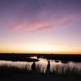 Two men stand silhouetted against a brilliant purple and orange sunset overlooking water on the conservation area of Gayini Nimmie Caira Credit Annette Ruzicka The Nature Conservancy