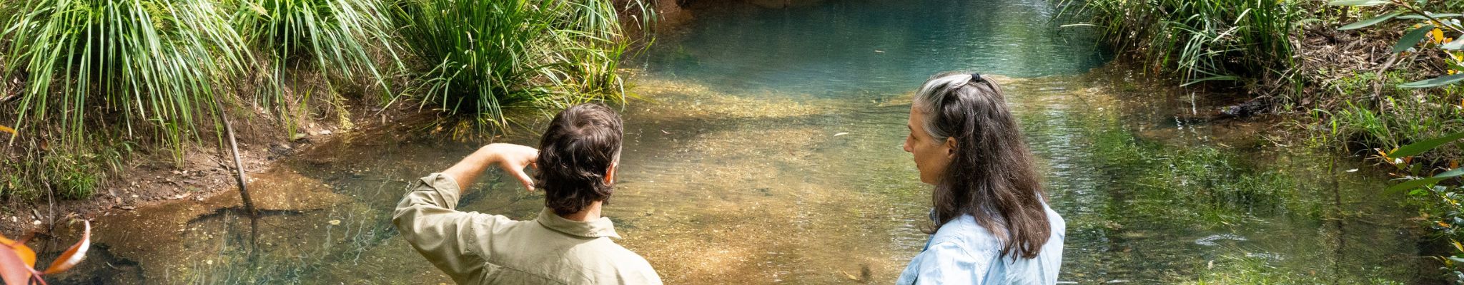 Man and woman stand on a creek bed looking over the water