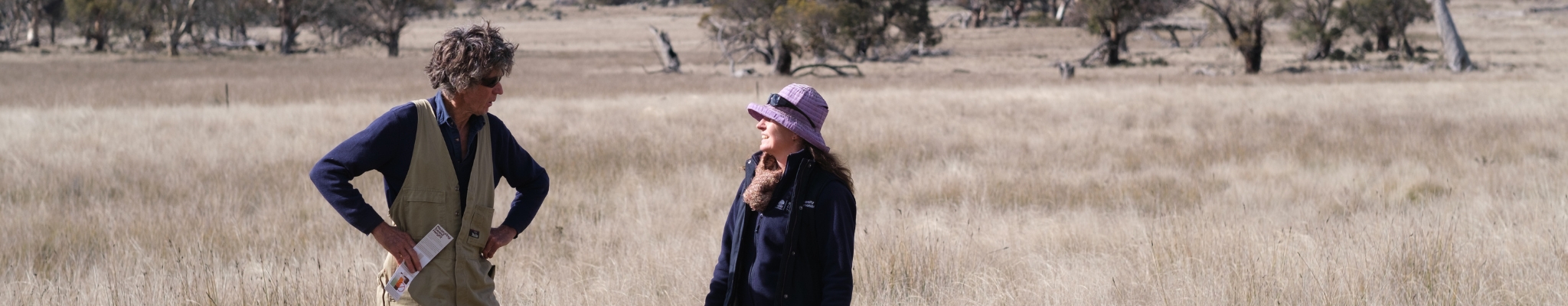 A landholder stands in a grassy paddock with a uniformed NSW Biodiversity Conservation Trust staff member