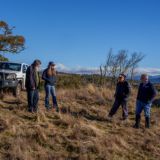 Four people stand aside a vehicle in a grassy and wooded paddock of a rural property