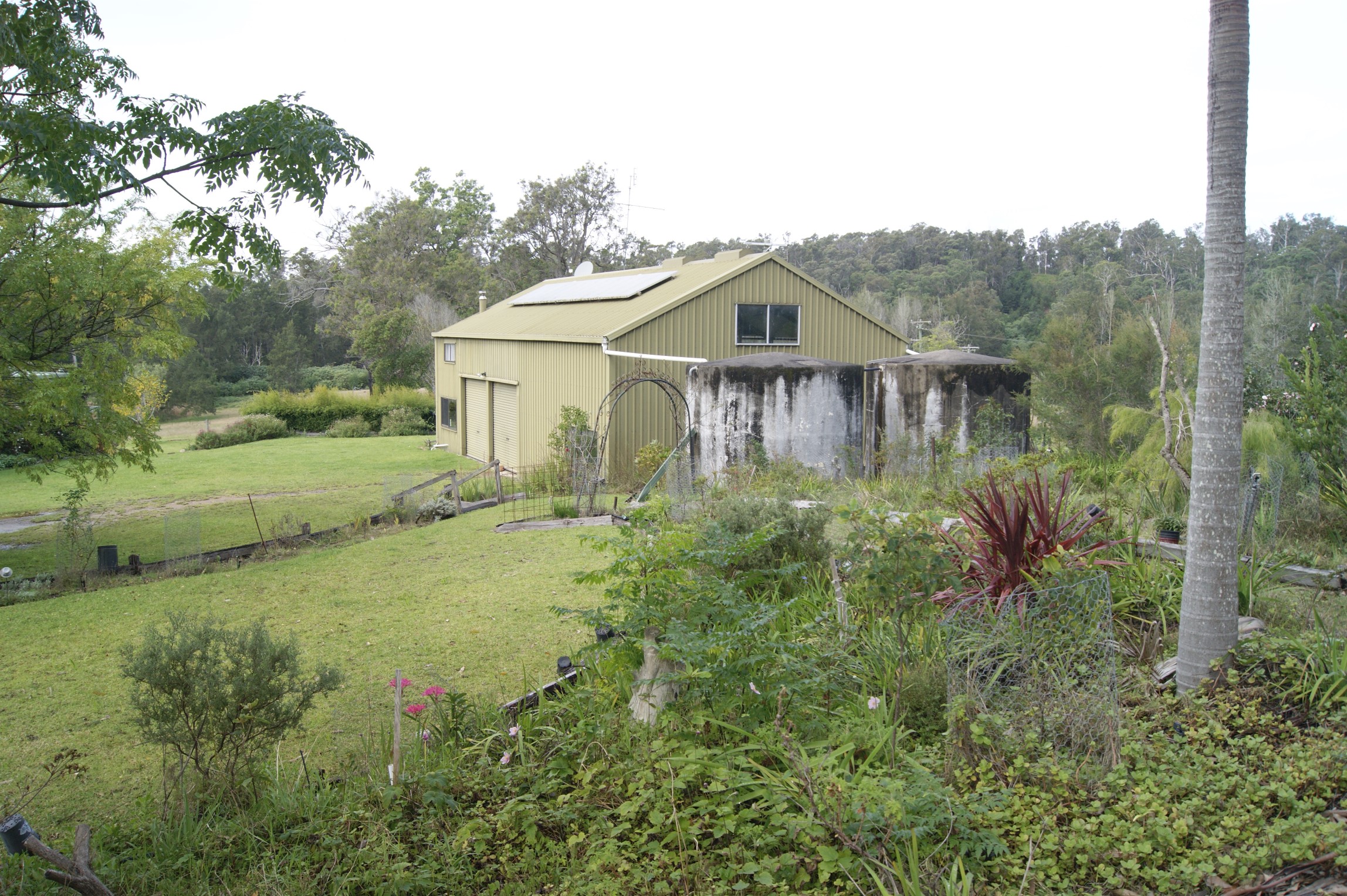 A side view of the olive coloured shed with two large rain water tanks